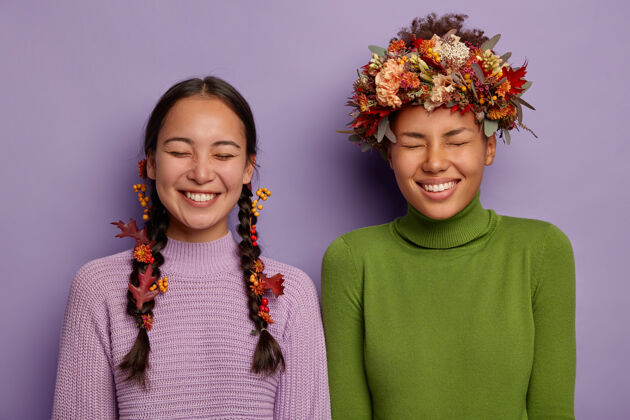 快乐两个快乐的女人是最好的朋友 一边欢笑一边拍照 用秋叶装饰头发 闭上眼睛 笑容灿烂 享受美好时光 紧紧地站在紫色的背景下牙线女孩亚洲