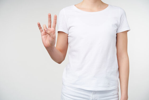 T恤不规则镜头中 女性举起手 用手指做手势 在手语中表示第七个 与穿着休闲服的白色背景隔离开来符号女人作物