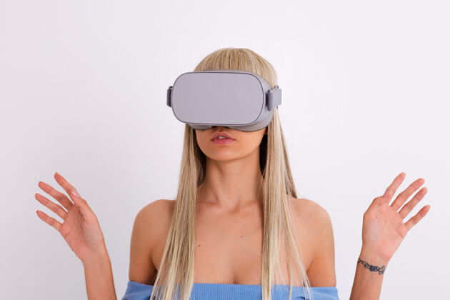 休闲摄影棚照片中一个年轻迷人的女子穿着温暖的蓝色时尚西装 戴着虚拟现实眼镜在白色的设备小玩意创新