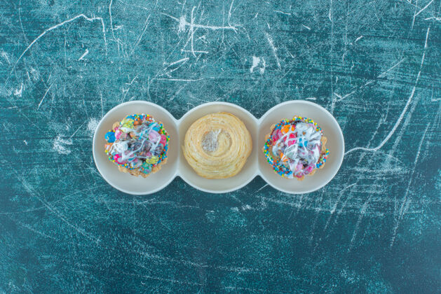 甜食杯子蛋糕和饼干放在蓝色背景的小盘子里高质量的照片糖果烘焙口感