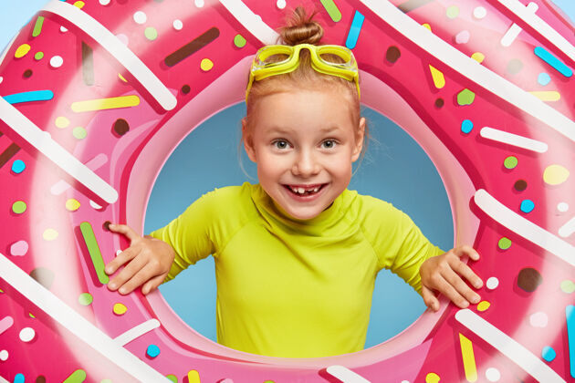 站开朗可爱的姜姑娘的特写肖像透过粉红色的橡胶圈把头伸进去 戴着护目镜和鲜艳的t恤 在海边度过暑假 喜欢游泳快乐的童年和休息休息穿红发