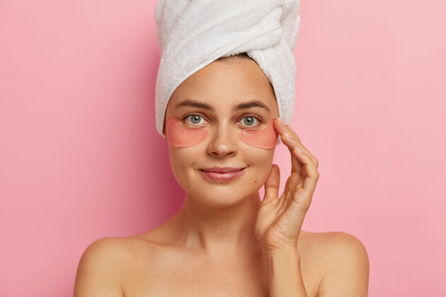 健康美丽的欧洲女性模特合拍拍淋浴后制作SPA程序 在眼部应用胶原蛋白贴片 有抗衰老治疗 站在室内头巾有趣化妆品
