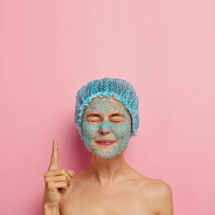 裸露满意的美女垂直形象脸上有蓝色海盐擦洗 闭上眼睛食指朝上 戴浴帽 周末在水疗沙龙有问题的皮肤干燥 美容制度女人人人