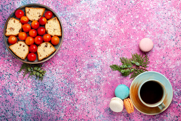 生的在粉红色的桌子上俯瞰美味的切片蛋糕和酸的新鲜李子麦卡龙和茶李子胡椒水果