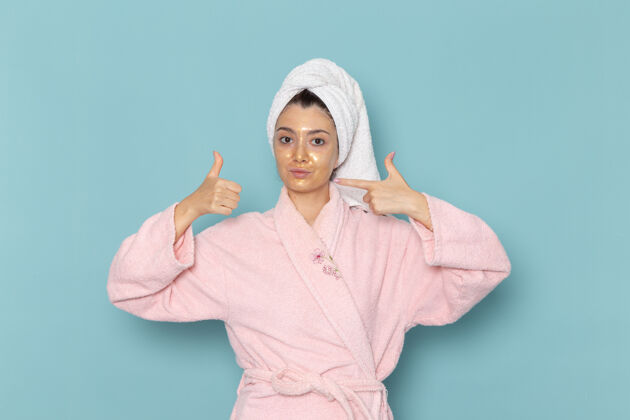 自我护理正面图身着粉色浴袍的年轻女性在浅蓝色墙壁上淋浴后 美丽的清水自理淋浴视图人浅蓝色