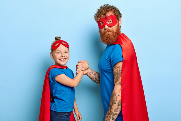 男性正女孩儿拉着胡子爸爸超级英雄的手红发携带斗篷