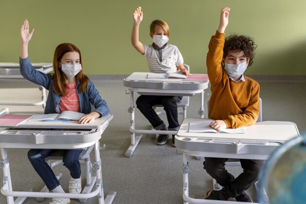 学习学校里戴着医用口罩的孩子们举手的正面图冠状病毒流行病返校