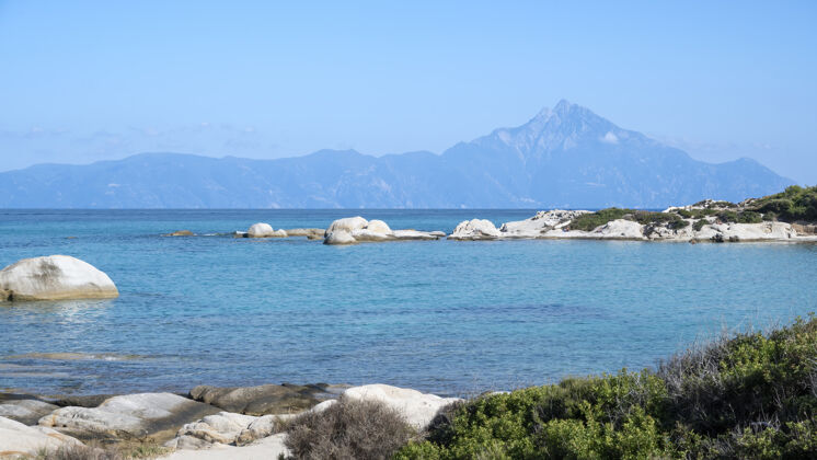 欧罗巴爱琴海海岸 水面上有岩石 远处有陆地 前景是绿色植物 蓝色的海水 希腊希腊山海滩