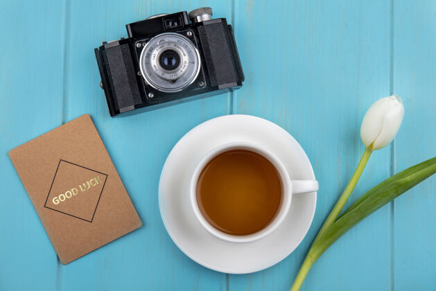 杯子茶碟和鲜花上的茶杯顶视图 蓝色背景上有照相\/摄像机和好运卡桌子杯子顶