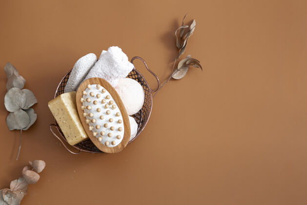 自然按摩刷 浴弹 肥皂和毛巾放在篮子里的棕色背景顶视图上木材化妆品浴弹