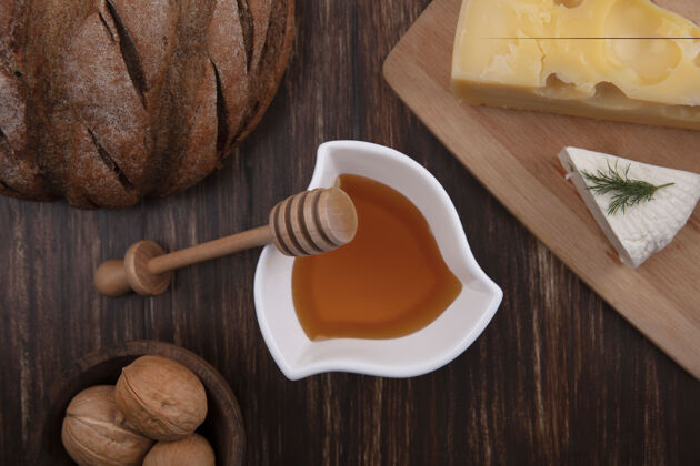 支架顶视图蜂蜜在一个碟子里 各种奶酪放在一个架子上 核桃和一条面包放在木制的背景上蜂蜜面包面包