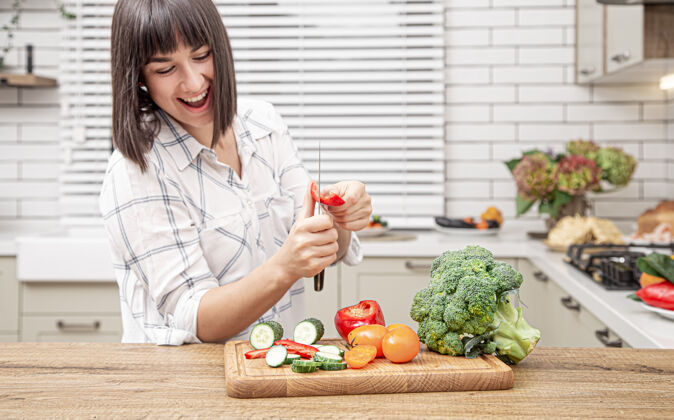 素食者在现代厨房内部的背景下 快乐的黑发女孩在沙拉上切蔬菜维生素年轻饮食