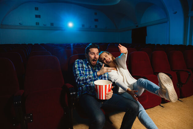 电影院迷人的年轻白种人夫妇在电影院 房子或电影院看电影看起来富于表现力 惊讶和情绪化独自坐着玩关系 爱情 家庭 周末时间吃夜生活男