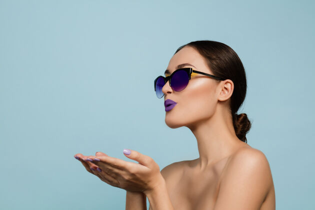 化妆美丽的女人的肖像 明亮的妆容和蓝色工作室背景上的太阳镜时尚 时尚的制作和发型夏天的颜色美丽 时尚和广告概念送吻眼睛女性太阳镜