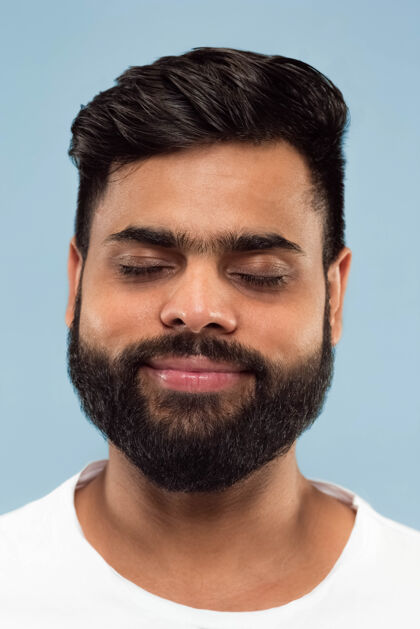 英俊在蓝色背景上孤立的穿着白衬衫 留着胡须的印度教年轻人的特写肖像人类情感 面部表情 广告概念负面空间闭着眼睛做梦手势胡须面部