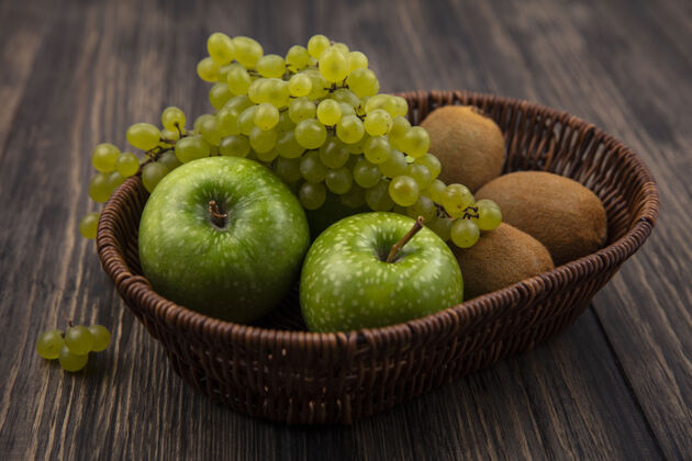 壁板侧视图绿色葡萄与苹果和猕猴桃在一个木制的背景篮子篮子木头植物