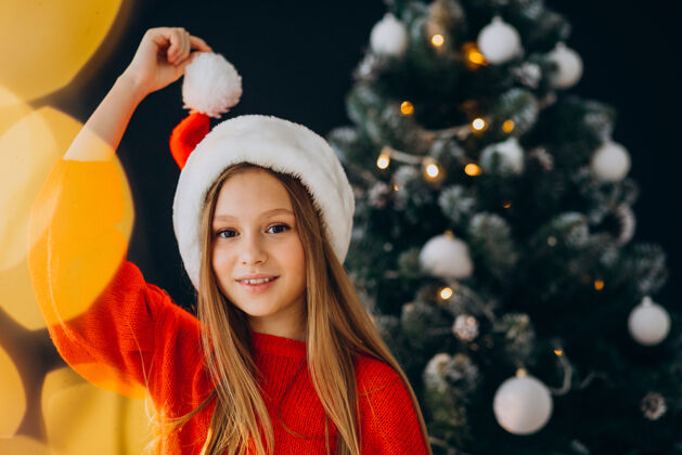 欢快可爱的少女戴着圣诞树旁的红色圣诞帽时尚年轻家