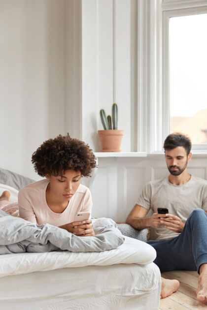 在线混血男朋友和女朋友阅读收到的通知 在卧室休息时发短信 忽视现场交流 表情严肃 关注手机成瘾和科技室内忽略上瘾