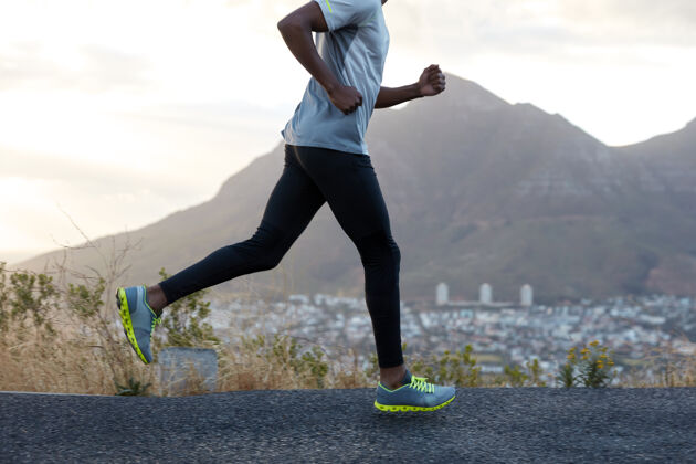 教练健康的黑皮肤男子在运动中 沿着山路奔跑 穿着舒适的运动鞋 休闲服 有运动的身体速度快的男运动员对着天空摆姿势赛车比赛户外慢跑人