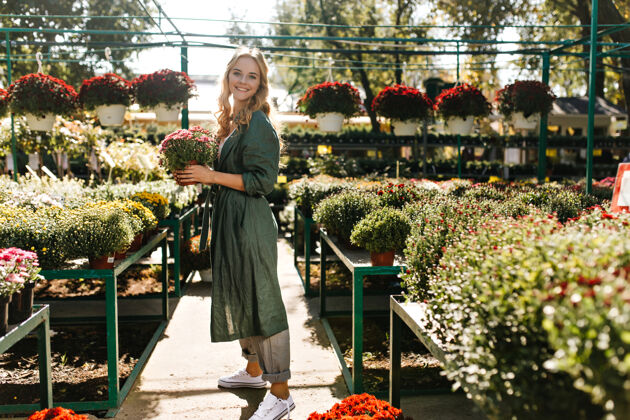成人一位金发碧眼 笑容温柔的年轻女子 身着绿色长袍 系着腰带 正在温室里工作可爱自然花园