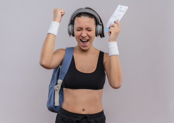 耳机年轻的健身女 头戴耳机 背着背包 手拿机票 握紧拳头站着运动装票