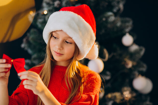 时尚可爱的少女戴着圣诞树旁的红色圣诞帽圣诞红帽子礼物
