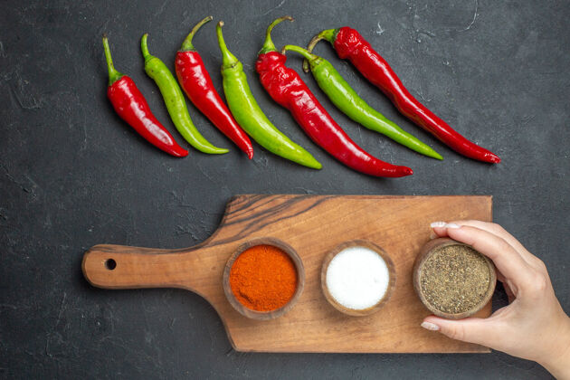 香料顶视图横排青椒和红椒不同的香料放在砧板上 女性手放在深色的表面上青椒和红辣椒板配料