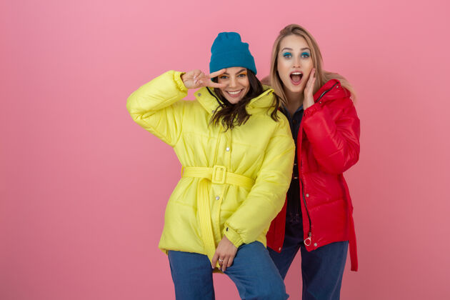 时尚两位魅力四射的女朋友穿着鲜艳的红黄相间的冬季夹克在粉色墙上自拍 一起玩乐 温暖的外套运动装时尚潮流 疯狂搞笑时尚秋天穿着