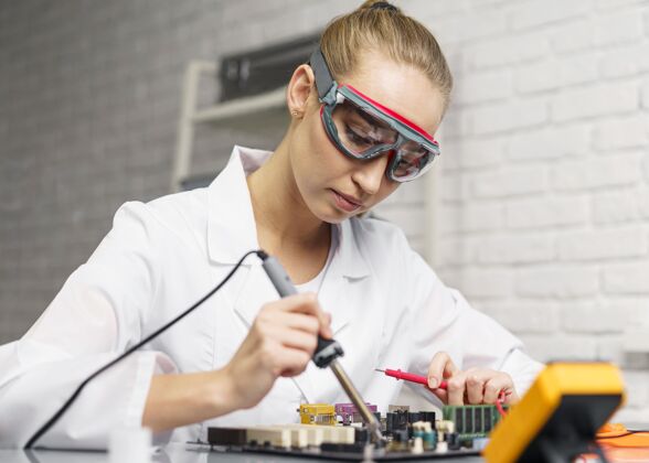 技术员女技师侧视图 带烙铁和电子主板发明家女实验室