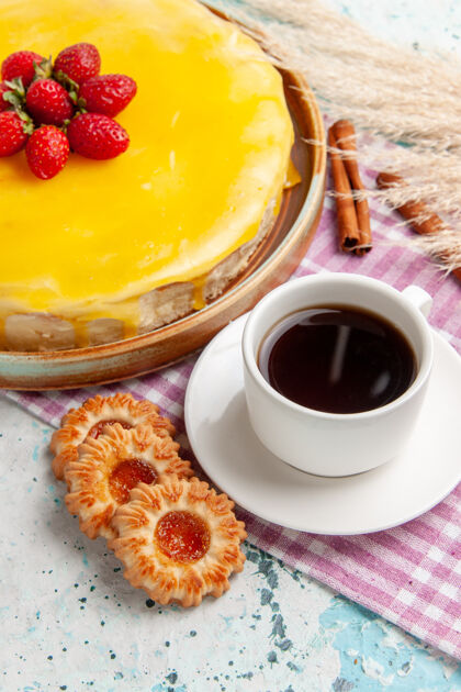 新鲜正面是美味的蛋糕 黄色糖浆 新鲜的红色草莓和一杯茶放在蓝色的表面派烘焙饼干
