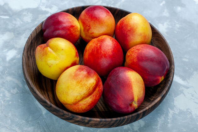 封闭正面近距离观看新鲜的桃子醇香可口的水果在浅白色桌子上的棕色盘子里桃子农产品核果