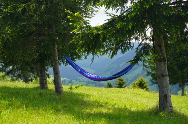 放松一张蓝色吊床的广角照片系在山上的两棵树上 可以看到美丽的自然景色美丽山自然