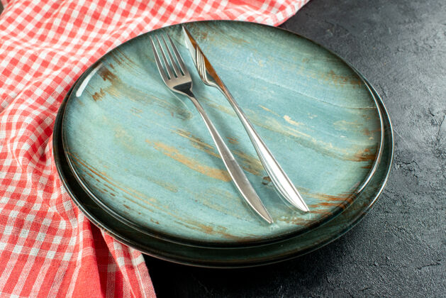钢底视图钢叉和餐刀在圆盘子上红白格子桌布在黑桌子上炒锅看法方格
