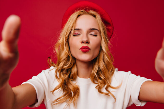 肖像有趣的法国女孩在红墙上摆出亲吻的表情可爱的金发女人戴着时髦的贝雷帽亲吻时尚成人