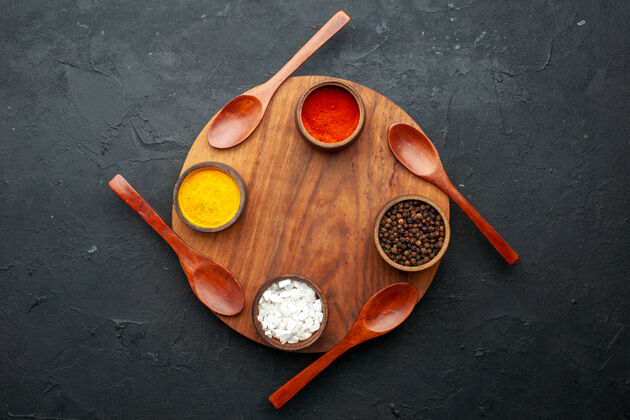 海顶视图姜黄红胡椒黑胡椒海盐装在小碗里四汤匙放在黑色桌子上的圆木板上 有复印空间姜黄黑碗