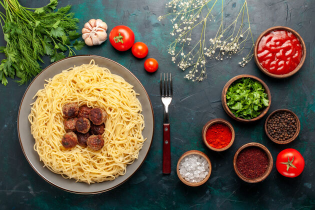 生的在深蓝色的桌子上俯瞰煮熟的意大利面食和肉丸调味料以及绿色蔬菜盘子奶酪肉