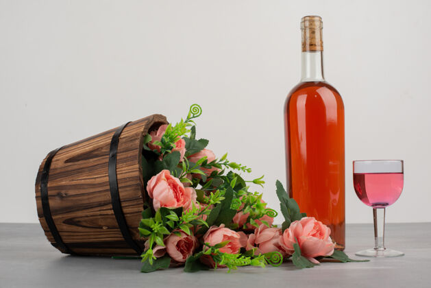 玫瑰美丽的花束和一瓶玫瑰红酒摆在灰色的桌子上花花束玻璃