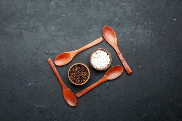 胡椒顶视图碗与海盐和黑胡椒围绕木勺在黑暗的桌子上与副本的地方地方深色木头