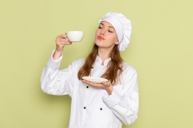 女性身着白色厨师服的女厨师正拿着一杯咖啡站在绿色的墙上烹饪微笑肖像