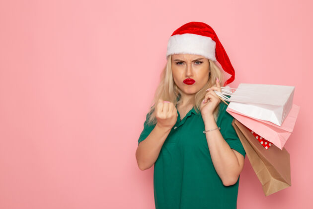 色彩正面图：年轻女性手拿圣诞礼物 包装在粉红色墙上的模型节日新年照片的颜色圣诞风景美丽