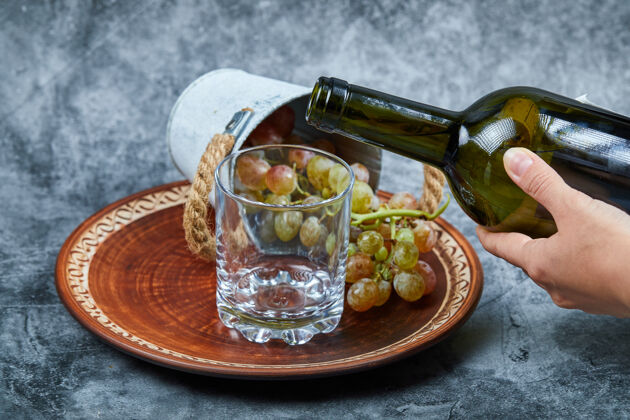 饮料小桶葡萄放在陶瓷盘子里 用手把葡萄酒倒进大理石上的玻璃杯里水果桌子桶
