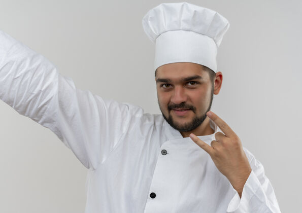 伸展高兴的年轻男厨师在厨师制服做摇滚招牌伸出手在一边孤立的空白做男制服