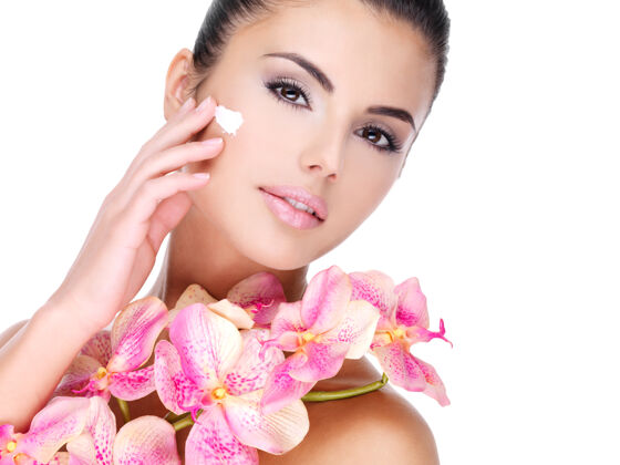 护理美丽的女人在脸上涂化妆霜 身体上有粉红色的花-隔离在白色皮肤护理皮肤人