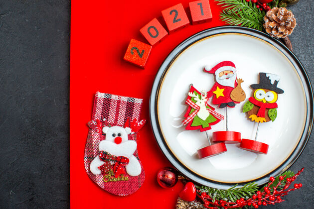 树枝餐盘装饰配件的俯视图杉木树枝和数字圣诞袜在一张黑色桌子上的红色餐巾上晚餐盘子碗
