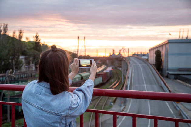 拍照一位年轻女子用手机在桥上拍摄美丽的日落铁路拍摄内容