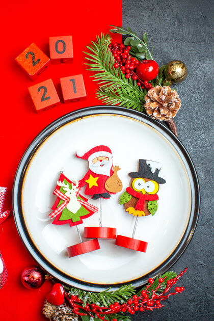 号码餐盘装饰配件的立面图杉木树枝和数字圣诞袜放在一张黑色桌子上的红色餐巾上晚餐盘子菜树枝