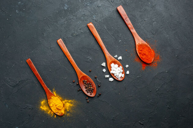 勺子顶视图斜排木勺 黑桌子上放着姜黄黑胡椒粉和盐红胡椒粉画笔木勺水