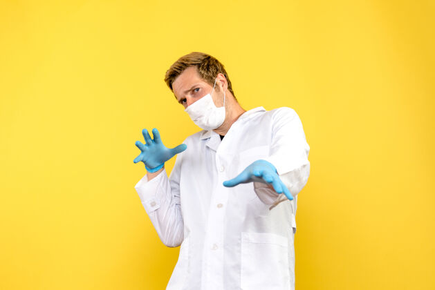 冠状病毒正面图黄色背景上戴面罩的男医生covid-大流行健康医生衣服视图正面