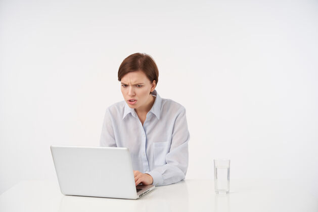 年轻困惑的年轻短发黑发女士的肖像 随意的发型看着笔记本电脑的屏幕 不高兴的脸 阅读不愉快的新闻 孤立的白色水笔记本电脑工作