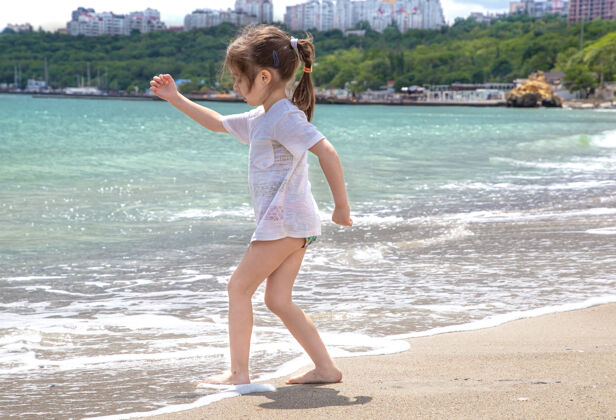 休息一个小女孩光着脚站在海边 在海浪中把脚弄湿了自然女孩沙滩